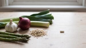 Garlic, onion, leeks, oats and asparagus on a wooden table beside a single plain capsule.