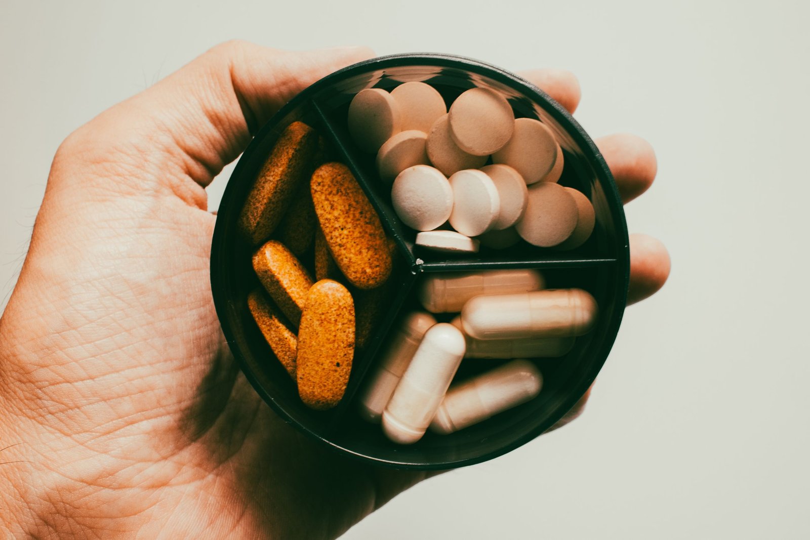 A hand holding several different supplement capsules, illustrating the choice of magnesium vs melatonin for sleep